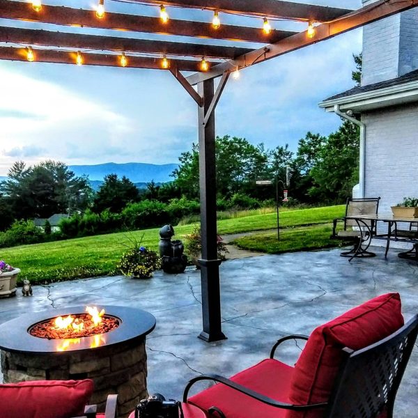 Comfortable outside seating area with fire pit table and a pergola with lights in the evening